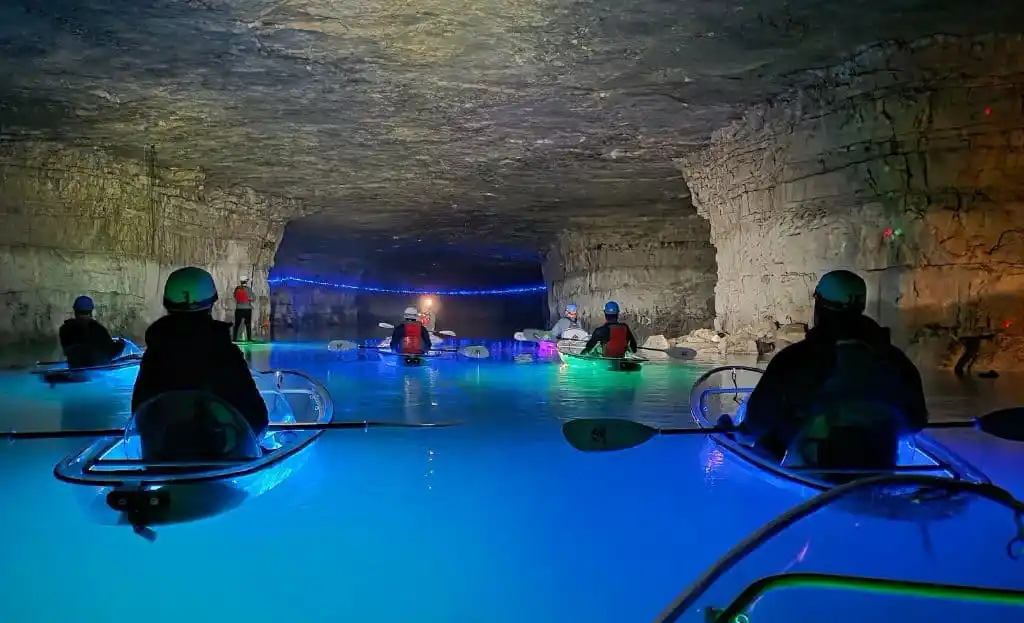 Clear-bottom kayaks on glowing blue water inside an underground cavern